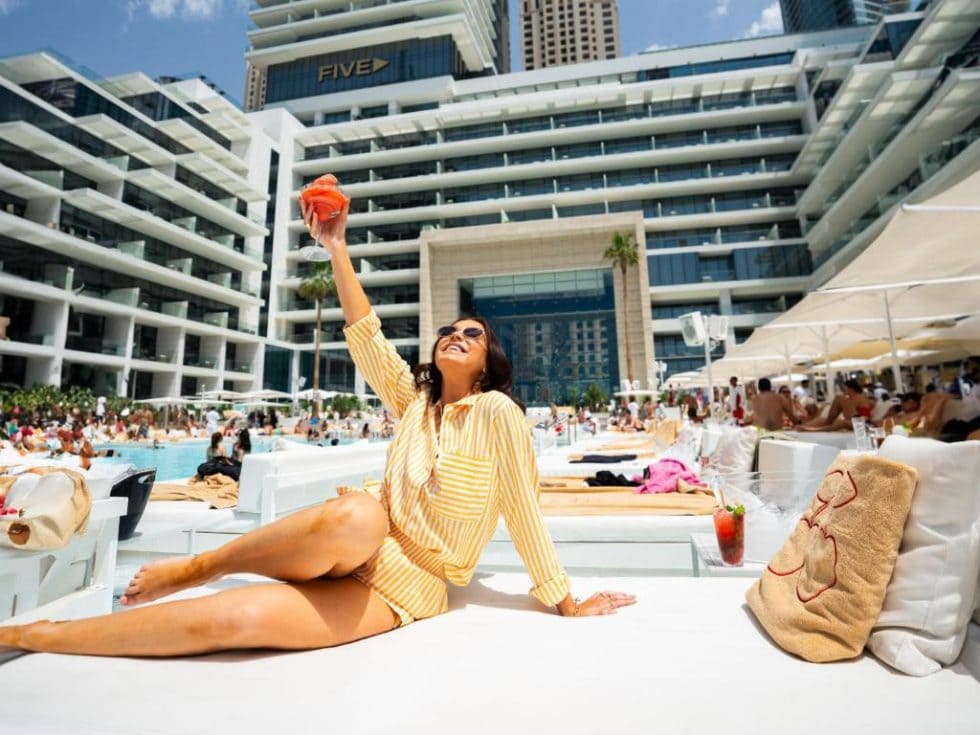 Escapade tropicale au bord de la piscine avec femme souriante en maillot jaune, hôtel moderne en arrière-plan, ambiance estivale, détente et plaisir en vacances.