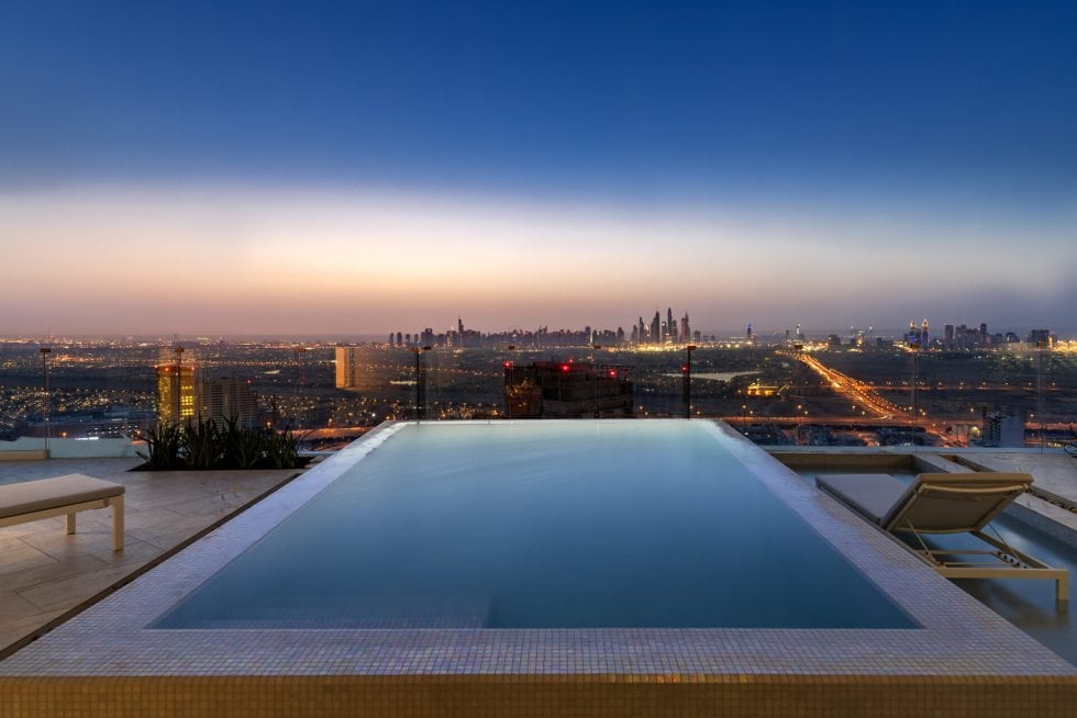 Vue panoramique d'une piscine à débordement sur un toit avec vue sur la ville illuminée au crépuscule, offrant un espace de détente luxueux et calme.