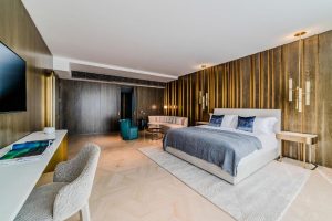 Luminosité intérieure d'une chambre d'hôtel moderne avec lit king-size, murs en bois, mobilier élégant, coin salon et espace de travail pour un séjour relaxant et confortable.