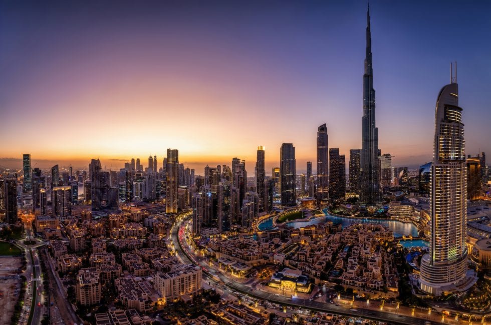 Vue panoramique du skyline de Dubaï au coucher du soleil, avec la tour Burj Khalifa illuminée, offrant une vue spectaculaire de la ville moderne et dynamique.