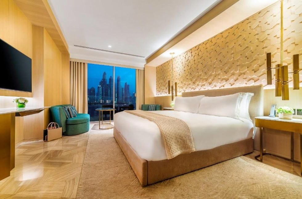Luxueuse chambre d'hôtel moderne avec lit king-size, décoration élégante en bois clair, vue sur la ville nocturne depuis la fenêtre, ambiance chaleureuse et confort haut de gamme.