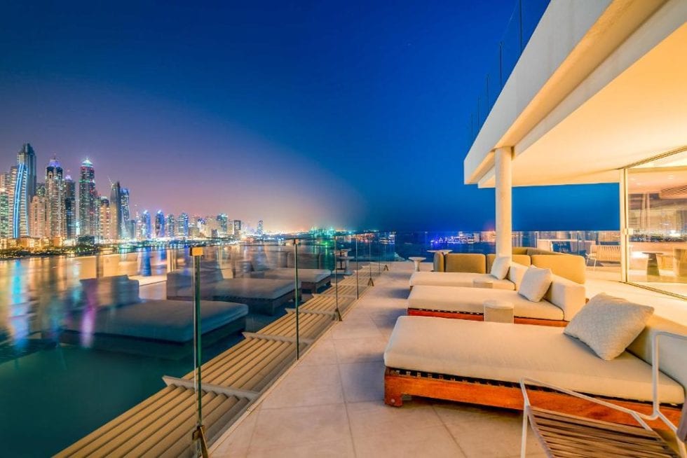 Vue panoramique sur la skyline de Dubaï depuis une terrasse en soirée avec mobilier moderne et vue sur la ville illuminée.